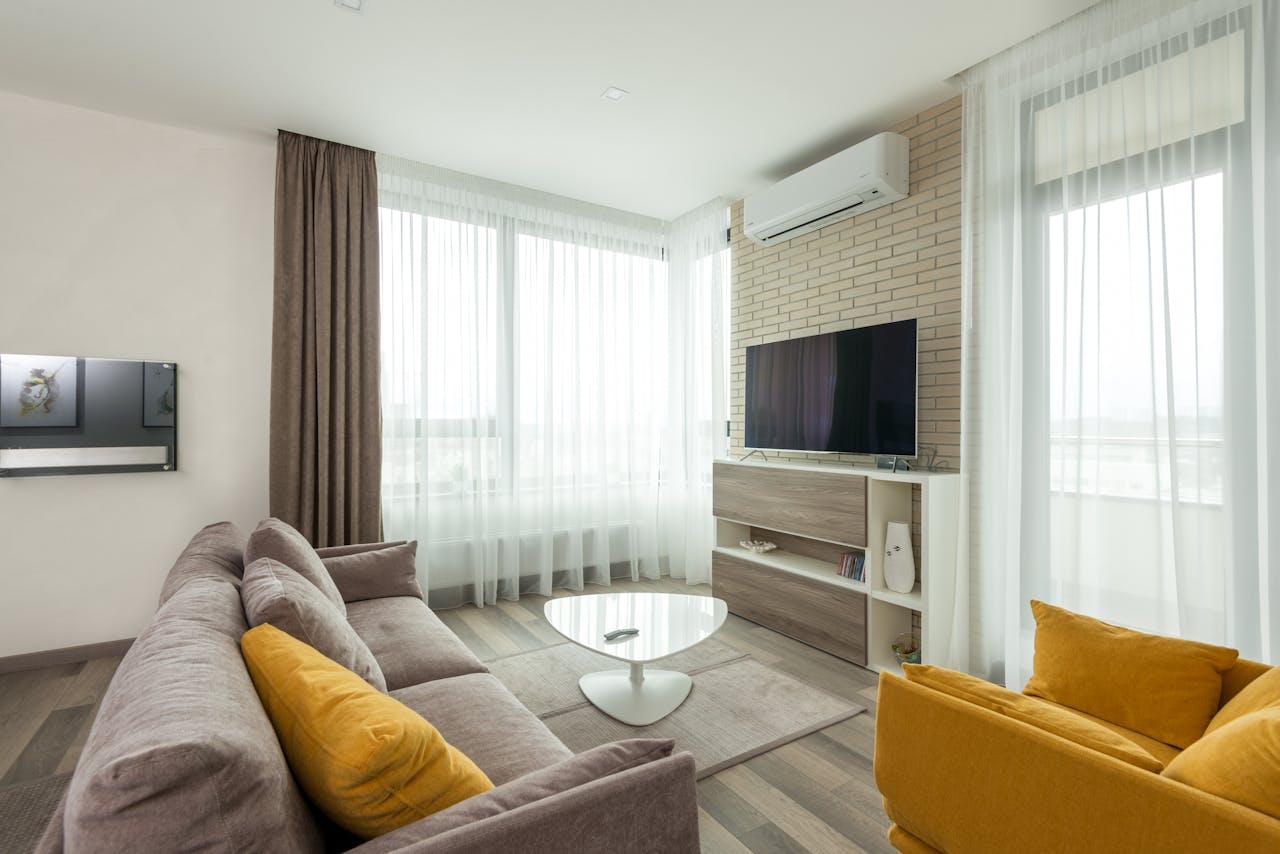 about-us-01 Soft comfortable sofa with cushions and armchair placed in front of TV hanging on brick wall in spacious living room of modern apartment